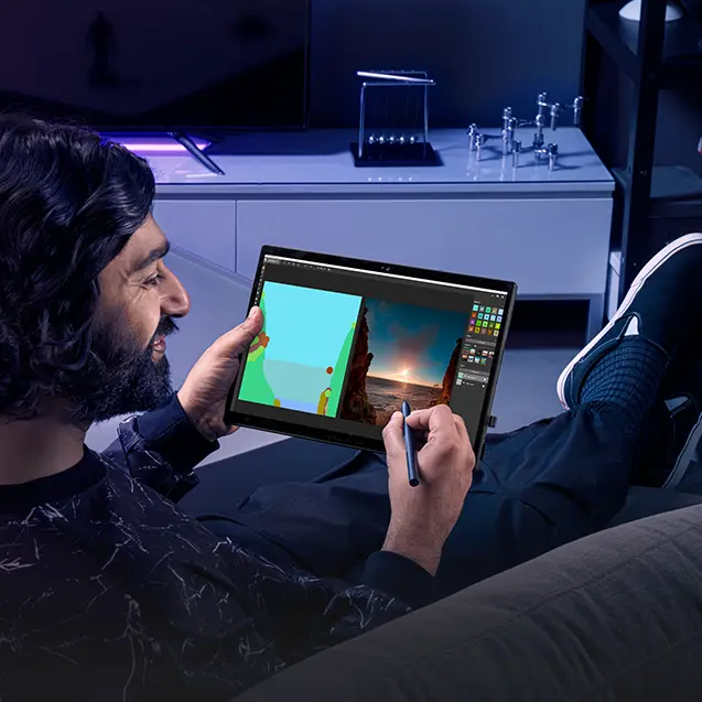 A person reclined on a couch, with the Flow Z13 and a stylus in hand abd drawing software on screen.